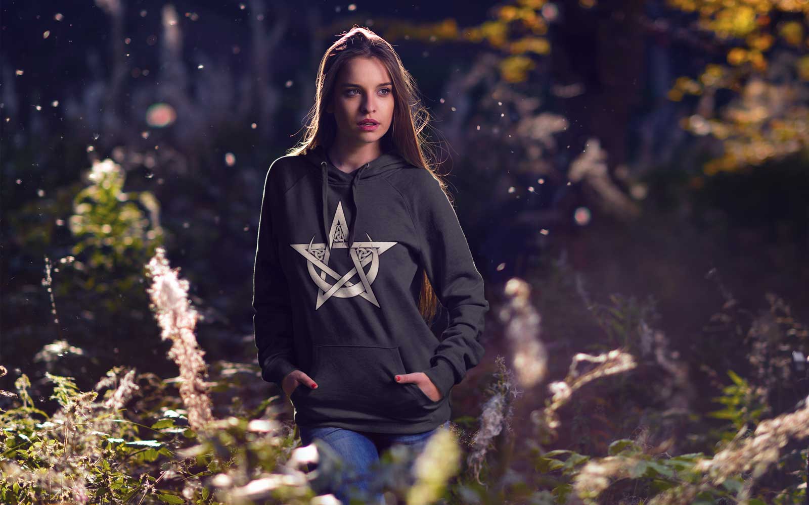a woman standing in a forest wearing a hoodie with a pentacle and crescent moon design 