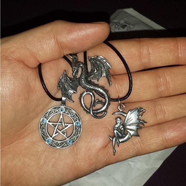 Product image showing a hand holding three necklaces. The first necklace features a pentacle pendant adorned with five birthstone crystals. The second necklace showcases a dragon pendant, while the third necklace depicts a faerie seated on a crescent moon. All pendants are connected to a leather cord.
